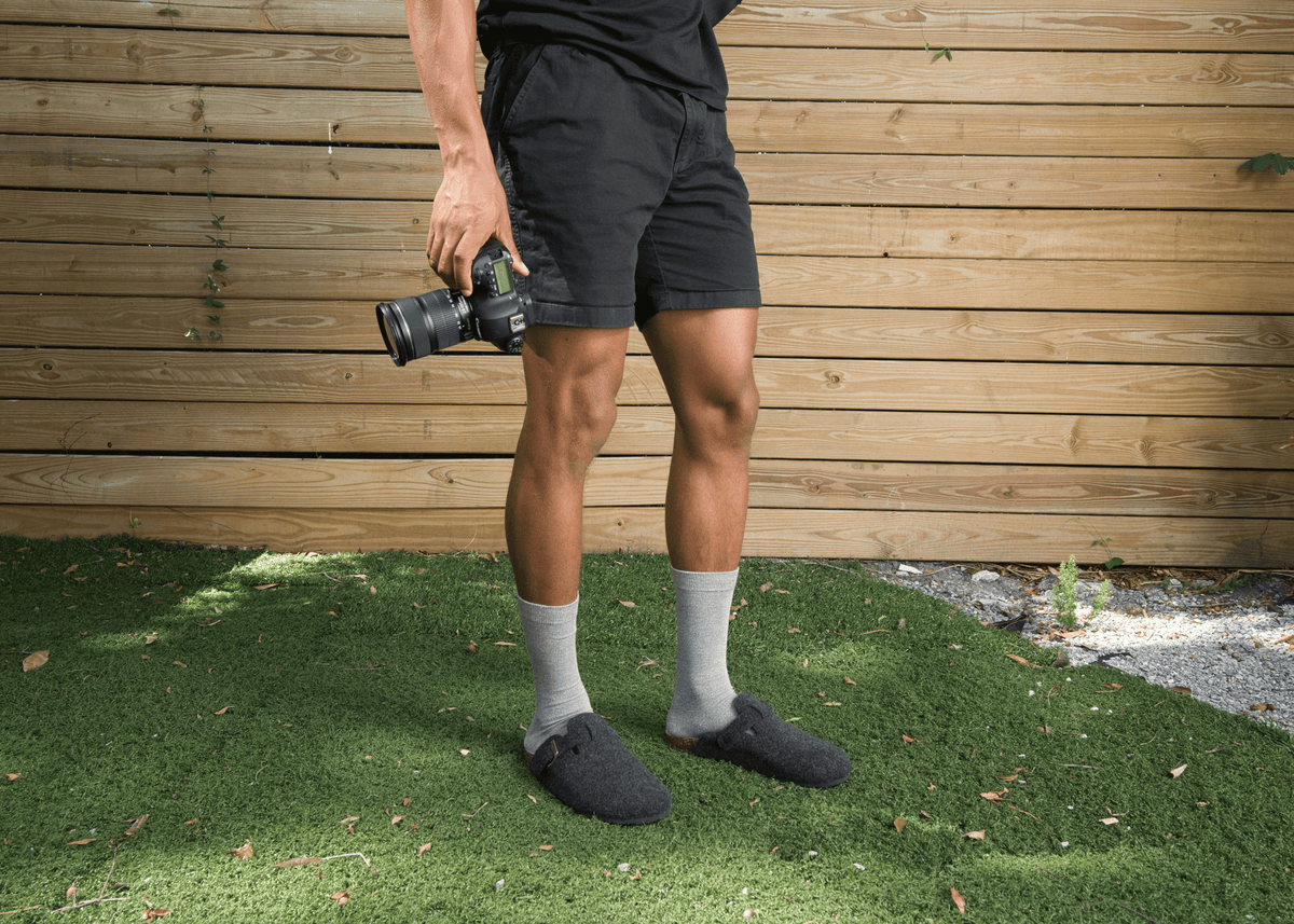 Person wearing black shorts and gray bamboo socks standing on grass with a wooden wall in the background