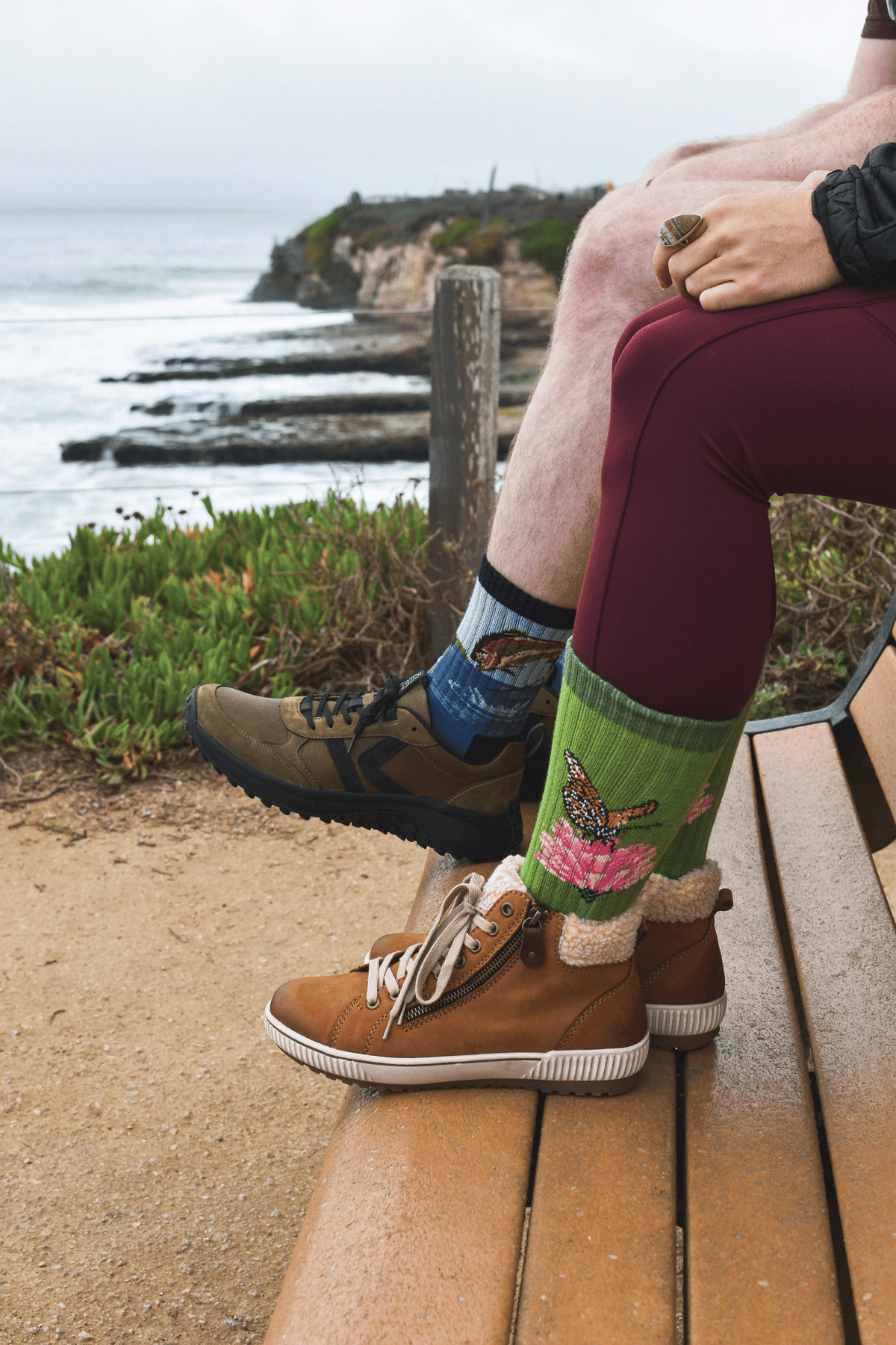 A close-up lifestyle shot of two people, one wearing fish-themed Merino wool socks and the other wearing Merino wool socks with a butterfly and flower on.