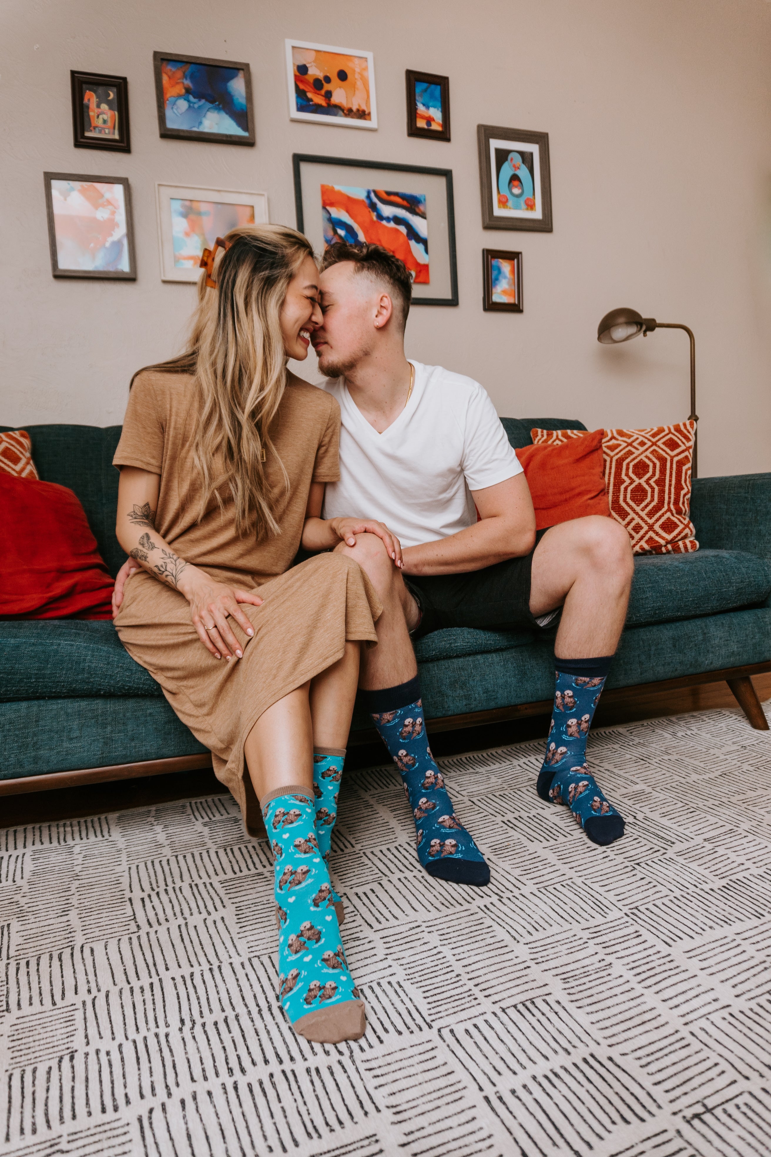 Couple sitting on a couch wearing colorful Significant Otter socks in a cozy living room.